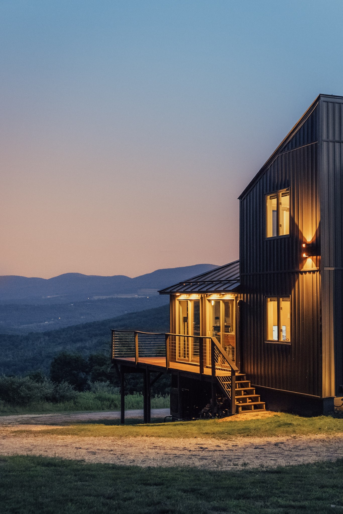 Front view of Hollow Sky at twilight — fireplace glowing, side deck, mountain backdrop