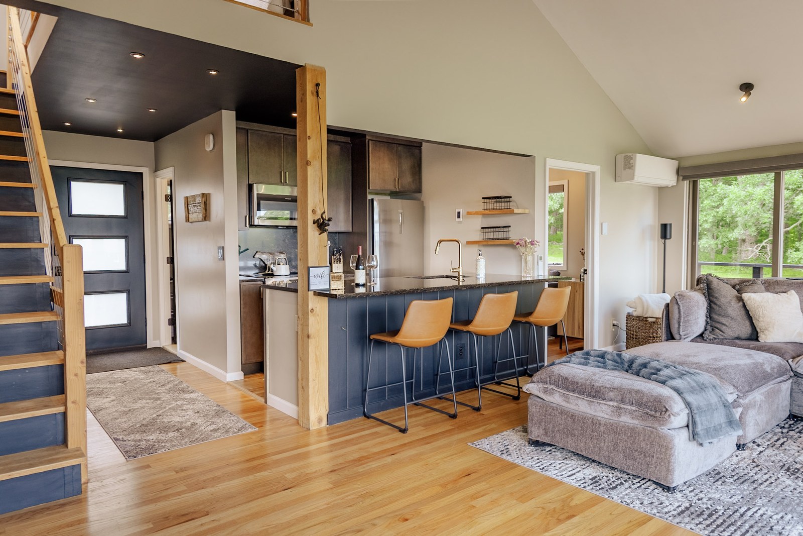 Open kitchen and living area with navy island, orange stools, and loft staircase